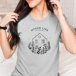 May include: Grey t-shirt with a black graphic of a house with windows and flowers, and the text "Hygge Life Find Simplicity."