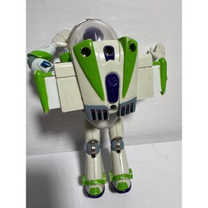 May include: A Buzz Lightyear action figure, featuring a white and green spacesuit design. The toy has a clear helmet, articulated arms, and a jetpack on its back. The figure is in a standing pose with its arms raised.