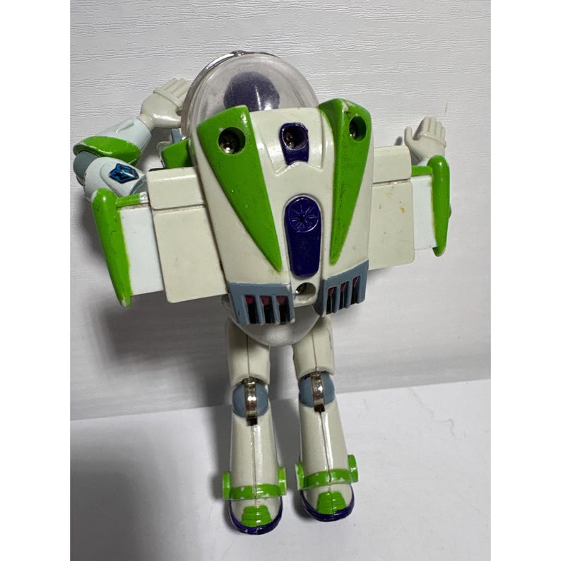 May include: A Buzz Lightyear action figure, featuring a white and green spacesuit design. The toy has a clear helmet, articulated arms, and a jetpack on its back. The figure is in a standing pose with its arms raised.