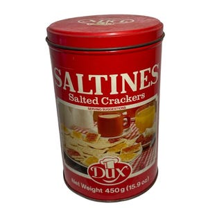Puede incluir: Lata roja y blanca con el texto "Saltines Salted Crackers" y una imagen de galletas saladas, una taza de café y un vaso de zumo de naranja. La lata también tiene el texto "Serving Suggestions" y "Dux" con un logotipo de gorro de cocinero. La parte inferior de la lata dice "Peso neto 450g (15,9 oz)".