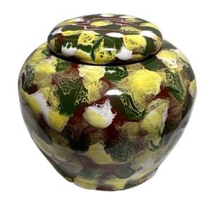May include: A ceramic jar with a lid, featuring a colourful pattern. The jar is adorned with yellow, green, white, and maroon shapes. It has a rounded body and a matching lid, suitable for storage.