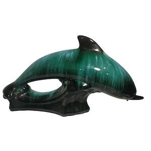 May include: A green and black glazed ceramic dolphin figurine. The dolphin is leaping out of the water with its tail raised. The glaze has a mottled effect, with shades of green and black.