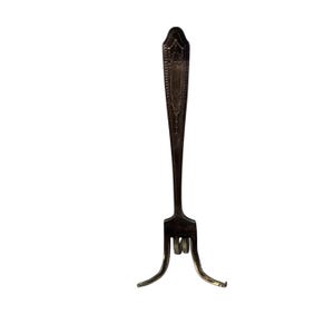 May include: An antique silver fork with a decorative handle and three tines. The handle features an ornate design, and the fork has two curved support legs. The fork is likely used for serving or displaying food.