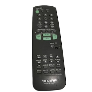 May include: A black Sharp TV-VCR-CATV remote control with green and white buttons. The remote has buttons for power, volume, channel, and playback controls. The model number G1494SA is visible.