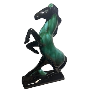 Könnte beinhalten: Keramikpferdefigur in aufbäumender Pose. Das Pferd hat eine glänzende Oberfläche mit schwarzem Kopf, Beinen und Sockel sowie einen leuchtend grünen Körper. Die Skulptur ist ein Dekorationsartikel, wahrscheinlich zur Präsentation.