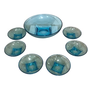 May include: A vintage serving set featuring a large oval bowl with a square base and six smaller bowls. The bowls are a transparent light blue color. The set is arranged on a white surface.