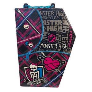 Può includere: Una borsa Monster High a forma di bara con un design a quadri neri, rosa e blu. La borsa presenta un design a cerniera, grafiche di teschi e le parole "Monster High" in vari caratteri.