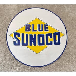 Könnte beinhalten: Rundes, weißes Schild mit blauem und gelbem Design. Die Worte "BLUE SUNOCO" sind in Blau, weiß umrandet, in einer gelben Raute dargestellt. Das Schild hat einen blauen Rand.