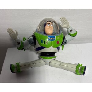 May include: A Buzz Lightyear action figure in a classic pose, with arms raised and legs spread. The toy features a green and white spacesuit with a clear helmet, and a smiling face. The figure is a collectible toy.