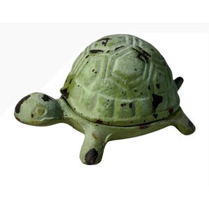 Könnte beinhalten: Eine Schildkrötenfigur aus Gusseisen mit einem abgenutzten hellgrünen Finish und dunkelbraunen Abnutzungsstellen. Die Schildkröte hat einen strukturierten, segmentierten Panzer, einen kleinen Kopf und vier Beine mit einer sichtbaren Naht zwischen Panzer und Basis.