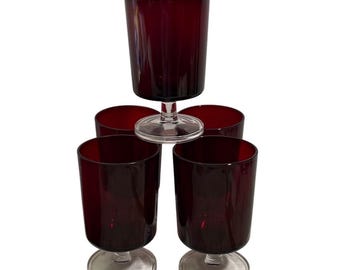 May include: Five ruby red stemmed glasses. Four glasses are arranged in a pyramid shape, with one glass balanced on top. The glasses have a clear, circular base and a cylindrical bowl.