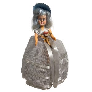 May include: A vintage doll with blue hair and a matching hat. The doll is dressed in a white satin gown with a net overlay and a ribbon sash. It holds a small bouquet of flowers. A collectible item.