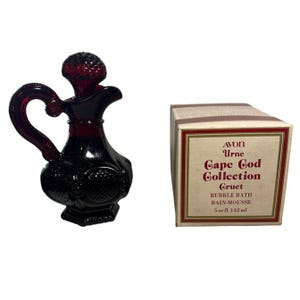 Könnte beinhalten: Eine dunkelrote Glas-Avon-Gruet-Parfümflasche mit Griff und Stopfen, neben einer Schachtel mit Cape Cod Collection-Schaumbad. Die Schachtel hat einen cremefarbenen Hintergrund mit rotem und goldenem Text.