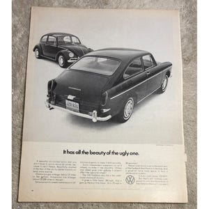 May include: Vintage black and white advertisement featuring two Volkswagen cars. The main car is a black fastback model, with a classic Beetle in the background. The text reads, "It has all the beauty of the ugly one."