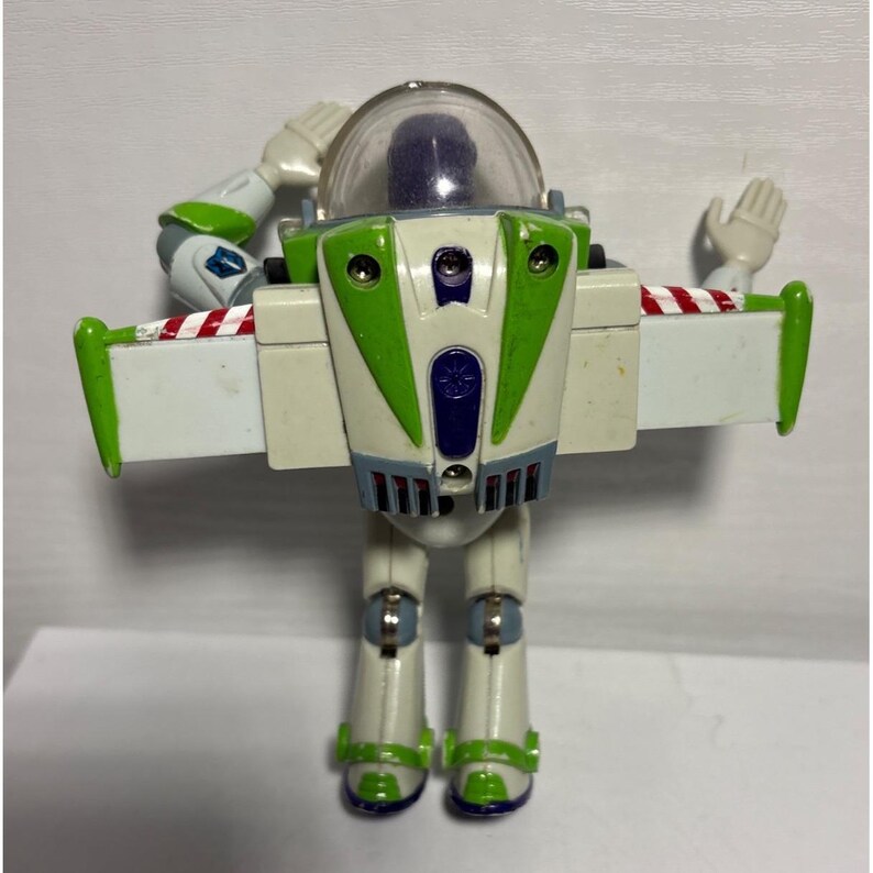 May include: A Buzz Lightyear action figure with a clear helmet, white and green body, and red and white striped wings. The toy is in a standing position with arms raised, showcasing its iconic design.