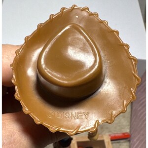 Puede incluir: Un sombrero de vaquero marr&oacute;n con un ala cosida y una corona redondeada. El sombrero est&aacute; hecho de un material liso y brillante. La palabra "DISNEY" est&aacute; impresa en la parte inferior del sombrero.