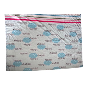Puede incluir: Una sábana de cama azul claro con un patrón repetido de nubes azules y el texto "Hello Kitty". El borde superior tiene rayas horizontales en rosa, rojo, azul y verde.