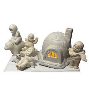 Puede incluir: Una escena invernal de cerámica con un iglú, un oso polar, una foca y varias figuras con ropa de invierno con capucha. Las figuras están en varias poses, una de ellas montada en el oso. El iglú tiene una ventana iluminada.