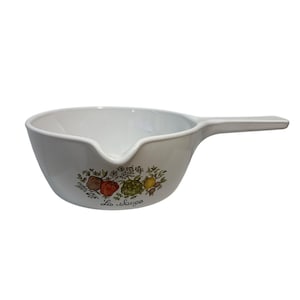 Może przedstawiać: Biały ceramiczny rondel z pojedynczym uchwytem i dzióbkiem do nalewania. Zewnętrzna strona ozdobiona jest kolorową ilustracją botaniczną ziół i warzyw, w tym czerwonego pomidora i zielonego karczocha, z nadrukowanym poniżej napisem La Sauge.