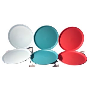 Peut inclure: Six plateaux de service colorés, blancs, turquoise et rouges, sont disposés sur un fond blanc. Les plateaux sont ronds et ovales, avec une finition lisse et mate. Les plateaux sont probablement en plastique ou dans un matériau similaire.