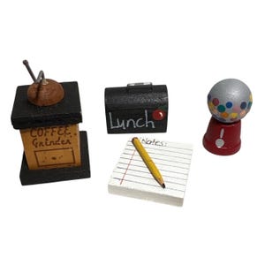 May include: A set of miniature wooden toys: a coffee grinder, a lunchbox with the word "Lunch", a notepad with a pencil, and a gumball machine. The coffee grinder has the words "Coffee Grinder" on it. The gumball machine is red and silver.