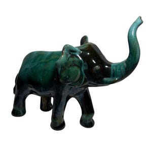 May include: A ceramic elephant figurine in shades of green and dark brown. The elephant has its trunk raised and is standing on four legs. The figurine has a glossy finish and is a decorative item.