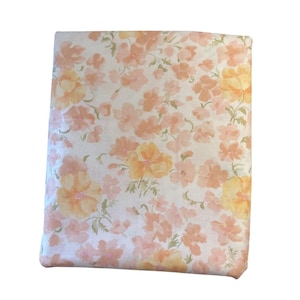 Może przedstawiać: Biała tkanina z kwiatowym wzorem w odcieniach brzoskwiniowego i żółtego. Kwiaty są w stylu akwarelowym i rozrzucone po tkaninie.