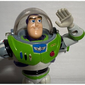 May include: Buzz Lightyear action figure in a green and white spacesuit with a clear helmet. The figure has a smiling face and is waving with its right hand. The word "LIGHTYEAR" is printed on the chest.