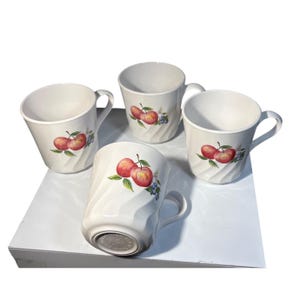 Può includere: Set di quattro tazze in ceramica bianca. Ogni tazza presenta un design di mele rosse e mirtilli con foglie verdi. Le tazze hanno un motivo strutturato e scanalato e un manico curvo.