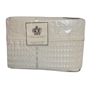 Peut inclure: Un drap plat blanc grand lit dans un emballage en plastique. Le drap est orné d'une bordure en dentelle blanche et porte l'inscription "Court of Versailles Cannon Royal Family" et "One King Flat Sheet".