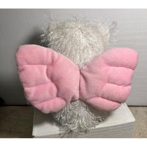 Op de afbeelding: Een witte teddybeer met roze engelen vleugels. De vleugels zijn gemaakt van een zacht, gewatteerd materiaal. De beer heeft een harige, getextureerde vacht. Het speelgoed is ontworpen als een troostrijk item.