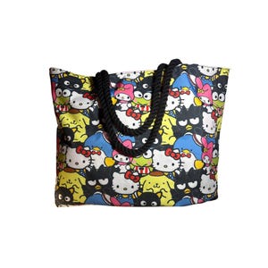 Puede incluir: Un bolso tote con un estampado colorido de varios personajes de Sanrio, incluyendo Hello Kitty, My Melody, Keroppi y Badtz-Maru sobre un fondo amarillo y azul. El bolso tiene dos asas gruesas de cuerda trenzada de color negro.