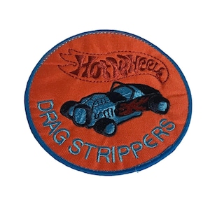 May include: Orange and blue embroidered patch with a Hot Wheels logo and a blue dragster car with the text "Drag Strippers".