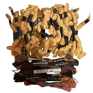 Könnte beinhalten: Eine Sammlung von Stickgarnen in verschiedenen Braun- und Beigetönen. Die Garne sind gebündelt und beschriftet, mit einer Mischung aus hellen und dunklen Farbtönen. Das Bild zeigt eine Vielzahl von Farben, von hellem Beige bis zu tiefem Schokoladenbraun.