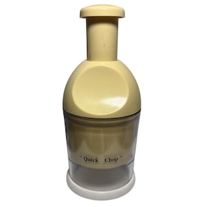 May include: A cream-colored manual food chopper with a clear plastic base. The chopper has a cylindrical design with a push-down mechanism and the words "Quick Chop" printed on the side. The base is white.