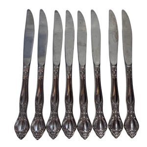 Könnte beinhalten: Satz von acht silbernen Essmessern mit verzierten Griffen. Die Messer haben eine polierte Oberfläche und sind mit einem dekorativen Blumenmuster verziert.