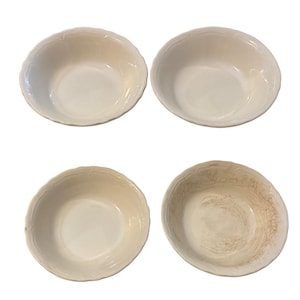 May include: Four off-white ceramic bowls with scalloped edges. The bowls are arranged in a square, with three bowls in good condition and one showing signs of wear. The bowls have a simple, classic design.