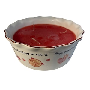 May include: A red candle in a white ceramic bowl with a scalloped edge. The bowl is decorated with the text "Sweet Things in Life" and "Fresh Baked Wishes". The candle has three wicks.