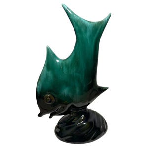 Può includere: Una statuetta a forma di pesce in ceramica nei toni del verde e del nero. Il pesce ha un design elegante e stilizzato con pinne prominenti e una base arrotondata. La finitura lucida esalta i dettagli.