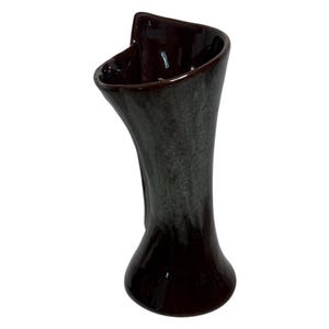 May include: A tall, ceramic vase with a unique, asymmetrical shape. The vase features a dark brown base that transitions to a gray and brown speckled finish. The top has a flared, curved opening. The vase is approximately 10 inches tall.