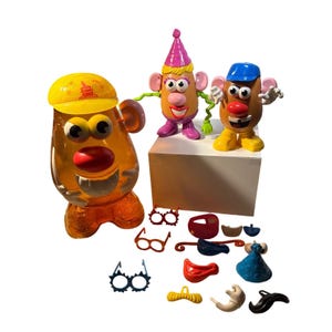 Puede incluir: Una colección de juguetes y accesorios de Mr. Potato Head. El conjunto incluye tres figuras con forma de patata con varios sombreros, junto con múltiples pares de gafas, bigotes y otros rasgos faciales. La figura principal es un recipiente naranja transparente.