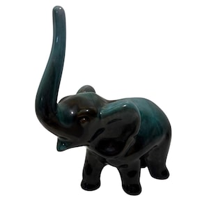 May include: A ceramic elephant figurine with a raised trunk. The elephant is glazed in shades of teal and black, with a glossy finish. The figurine has a detailed trunk, ears, and legs, and is a decorative item.