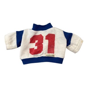 Könnte beinhalten: Ein weiß-blaues Puppen-Sweatshirt im Vintage-Stil mit der roten Nummer 31 auf der Vorderseite. Der Pullover hat blaue Verzierungen an Kragen, Ärmeln und Saum. Die Ärmel sind kurz.