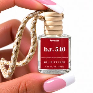 May include: A small clear glass oil diffuser bottle with a wooden cap and a beige and gold braided hanging cord. The red label features the text femme luxe, b.r. 540, saffron | jasmine | fir resin | amber | cedarwood, OIL DIFFUSER, and 0.33 FL. OZ (10 ML).