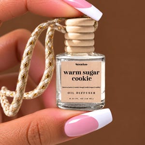May include: A small clear glass oil diffuser bottle with a light wood cap and a beige label. The label reads femme luxe, warm sugar cookie, brown butter, cookie dough, milk, sugar, vanilla, OIL DIFFUSER, and 0.33 FL. OZ (10 ML). A braided cord is attached.