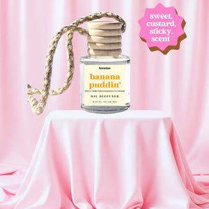 May include: A clear glass oil diffuser with a wooden cap and a braided rope. The label reads "banana puddin'" and "OIL DIFFUSER". The scent is described as "sweet, custard, sticky". The bottle contains 0.33 fl oz (10 ml).