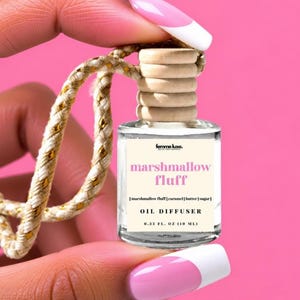 May include: A small clear glass oil diffuser bottle with a light wood cap and a beige label. The label reads femme luxe, marshmallow fluff, marshmallow fluff | caramel | butter | sugar, OIL DIFFUSER, and 0.33 FL. OZ (10 ML). A gold-flecked rope is attached.