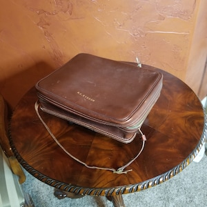 May include: A brown leather travel case with a zipper closure and a strap. The case has the text "R.L. Ellison" embossed on the front.