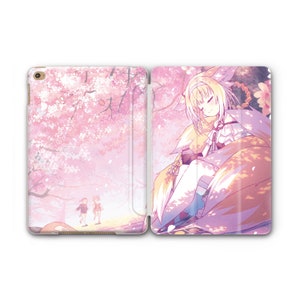 May include: A pink and white iPad case with a design of a girl with blonde hair and a fox tail sleeping in a field of cherry blossoms. The back of the case features a pink and white cherry blossom tree with two people walking in the background.