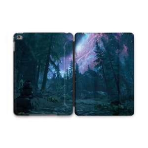 May include: An iPad case featuring a scenic forest landscape under a starry night sky. The design showcases tall trees, a winding path, and a vibrant display of stars and nebulae in shades of purple, blue, and white. The case is open, revealing the device's screen.
